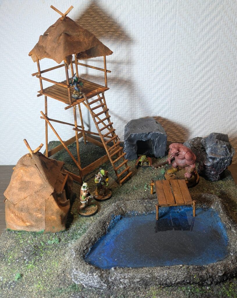An orc hut with two orc warriors in front of it, a pond, a troll near a bloody stone, a cocatrix near a grotto, a wooden tower with a gobelin in it.
