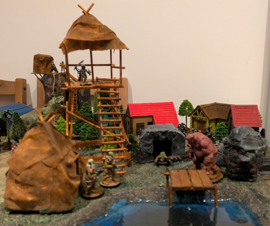 A miniature terrain with a hut, a tower, a grotto, a lake, and some monsters like orcs, troll, gobelin, cocatrix