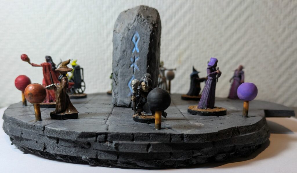The top of a mage tower, with nine wizards facing crystal balls. Every mage has its own colour theme, matching his/her crystal ball. An illithid is climbing stairs.