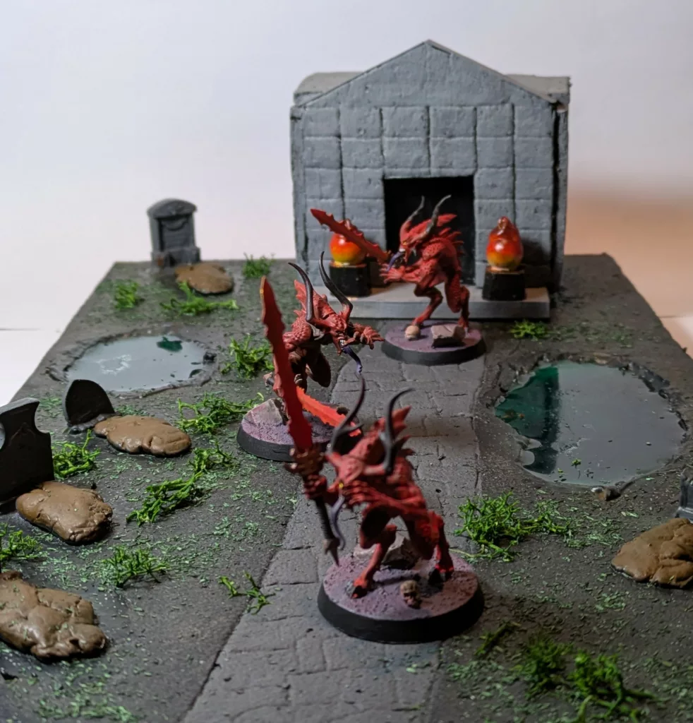Three Warhammer 40K Chaos Daemons Bloodeletters on a handmade cemetery with a few tombs, a crypt and two ponds of green water.