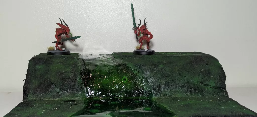Two Warhammer 40K Chaos Daemons Bloodletters standing on a green terrain that looks like a wet green blight, made with XPS foam.