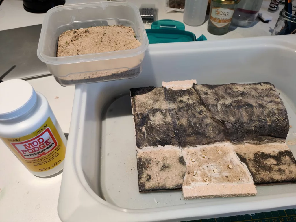 A miniature terrain made of XPS foam and isolation foam, covered in black mod podge and sand.